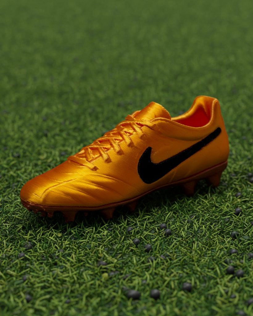 Gold soccer cleat with black Nike logo on a white background