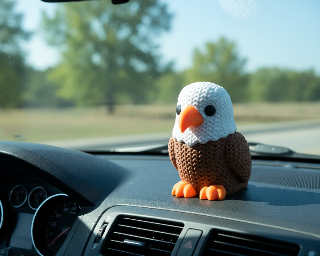 Crocheted eagle toy with white head, brown body, and orange feet and beak on a light gray background